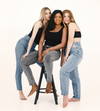 Three women wearing jeans and black tops posing together on a white background